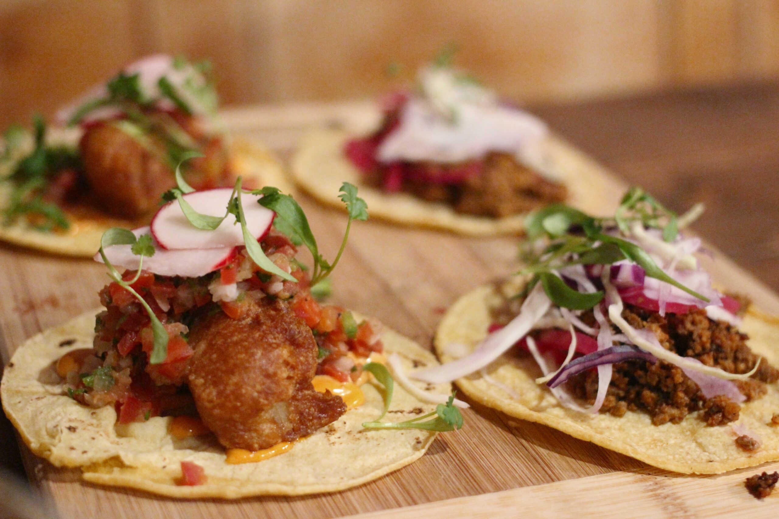 Four tacos on a wooden tray