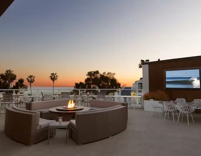 Outdoor Rooftop Lounge for Food and Cocktails with Firepits, Large Seating Areas, A Flatscreen TV, and Panoramic Ocean Views at Sunset