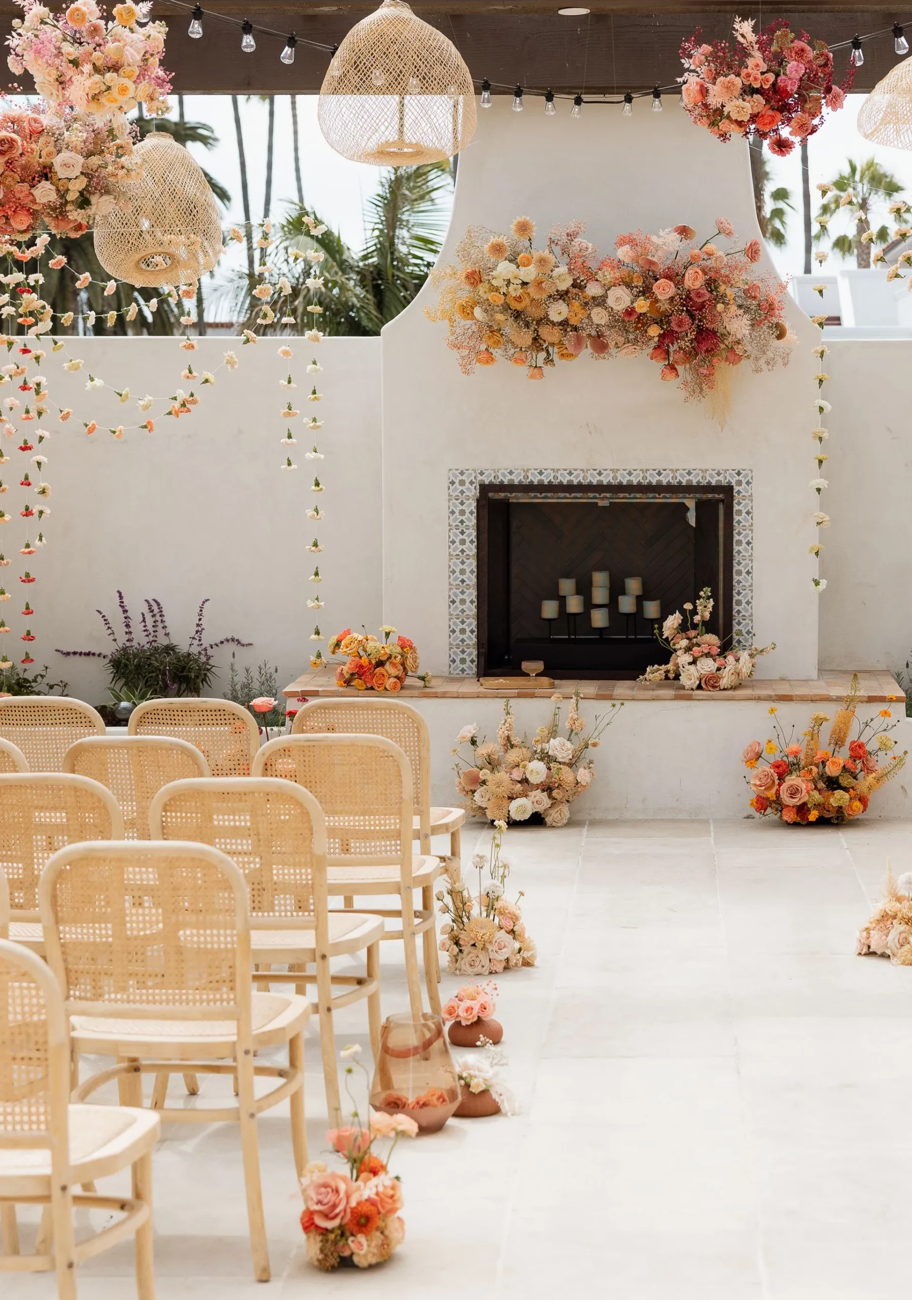 Peach and Pastel Colored Floral Arrangements at a Wedding Venue with Fireplace, Hanging String Flowers, and Seating from Wildflower Florist in Capistrano Beach