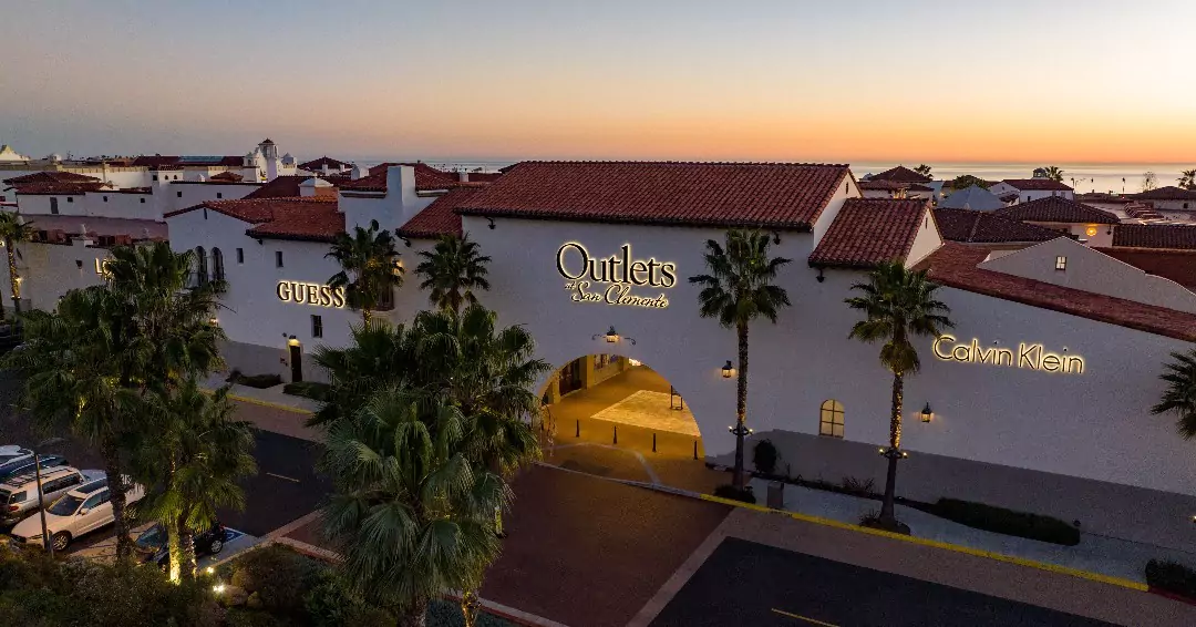 Aerial View of the Outlets at San Clemente with a Guess Store and Calvin Klein at Dusk, with Palm Trees and Parked Cars in the Foreground