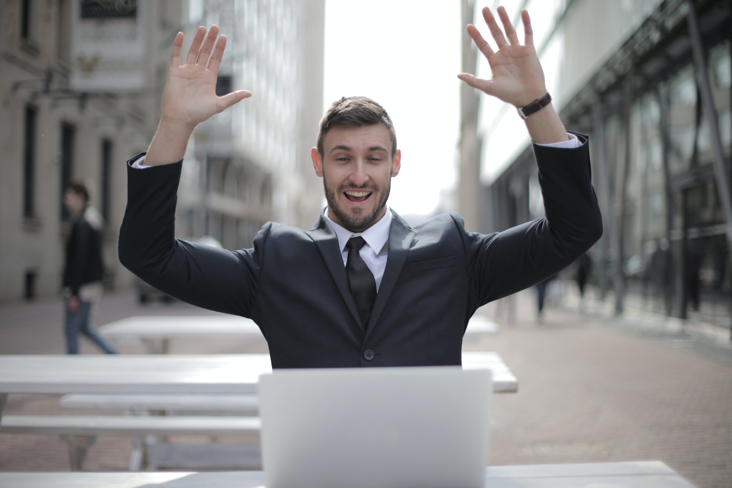 Confident businessman in black suit with raised hands representing rising consumer confidence in Orange County's real estate market.