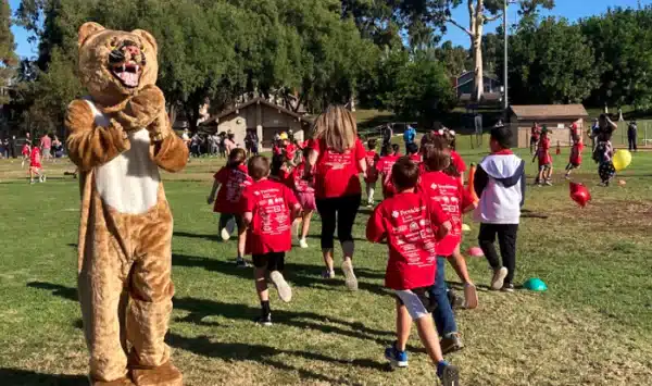 elementary school students in red shirts running outside by school mascot at brea country hills elementary school