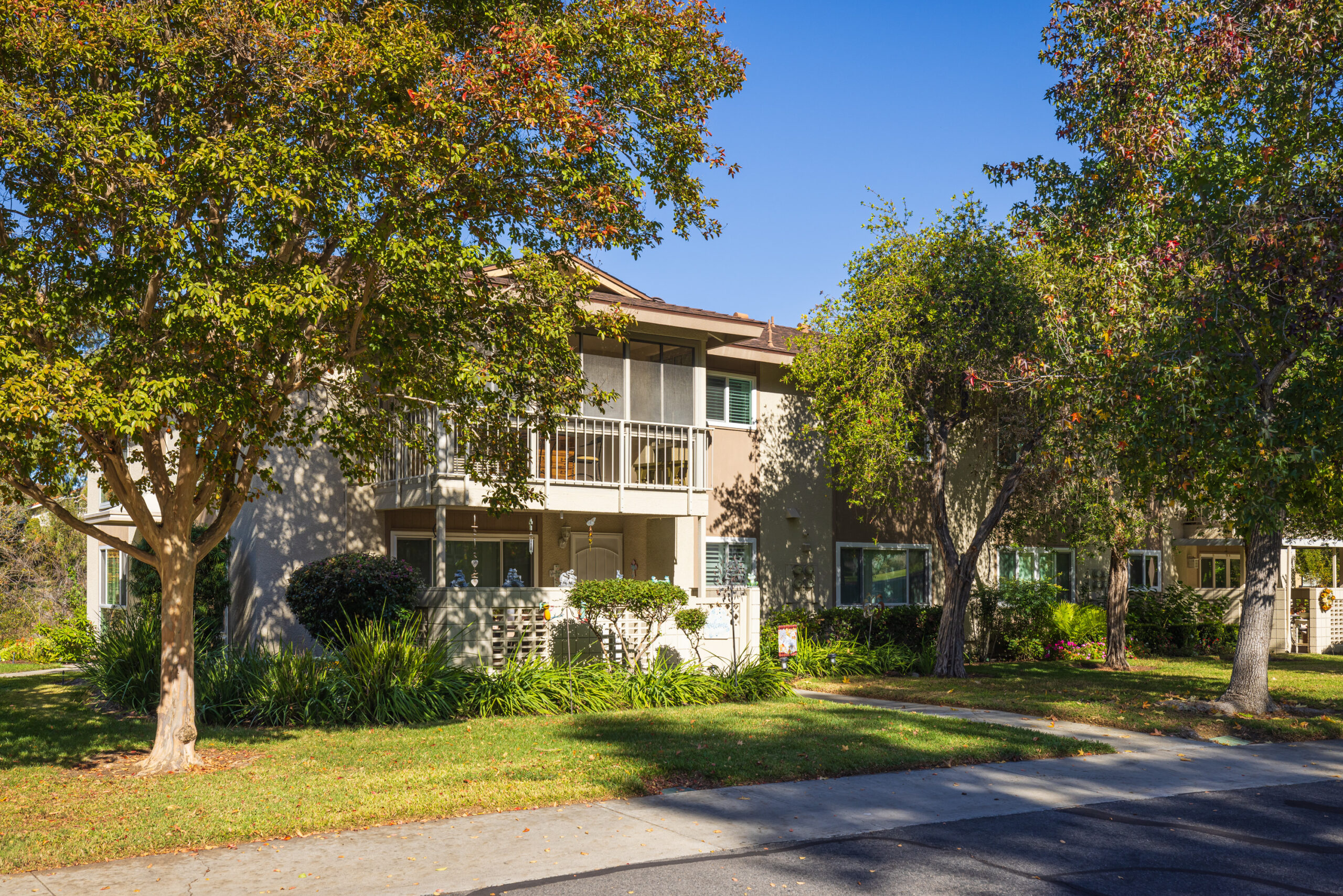 Exterior view of a sunny Laguna Woods condo surrounded by trees