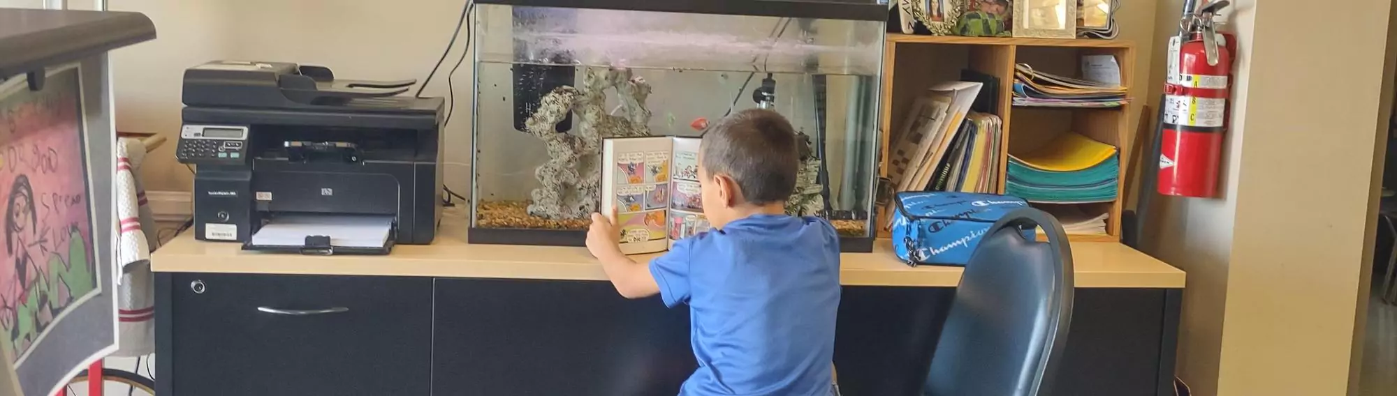 Elementary Student in light blue shirt Reading a Picture Book and Feeding the School Fish at Clara J. King Elementary