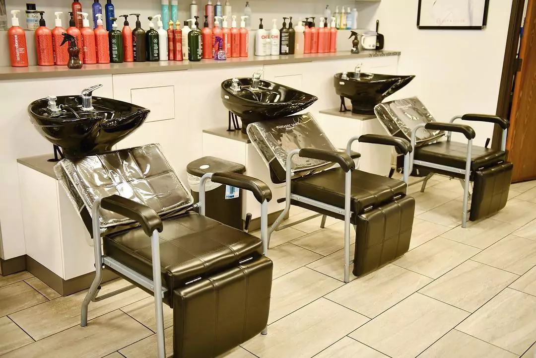 Picture of three Salon Chairs and Shampoo Stations with a Shelf Full of Haircare Products in Background