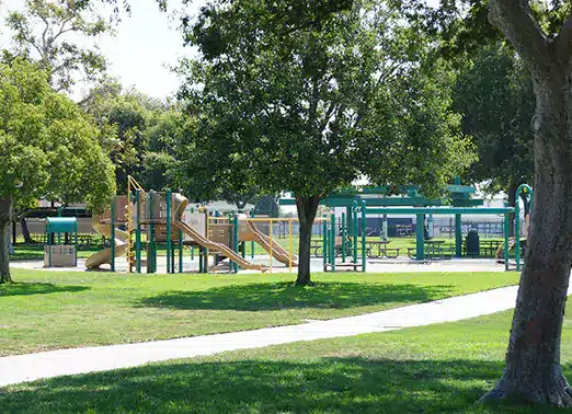 Long Sidewalk, Open Grassy Area with Trees, Playground, and Picnic Tables in the distance at Oak Knoll Park