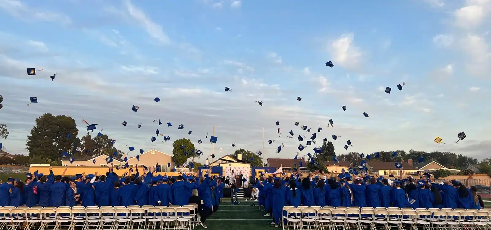 Graduating Class of High School Seniors in Blue Gowns throwing their caps in the air at El Toro High School