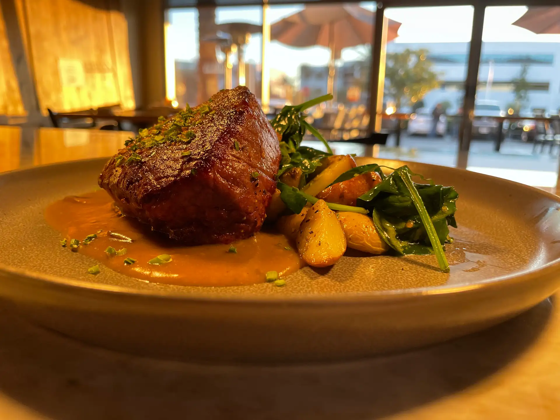 Plate with Filet Mignon, Roasted Potatoes, and Sauteed Spinach with Blurred View of Restaurant and Patio in Background at Urban Grill and Wine Bar