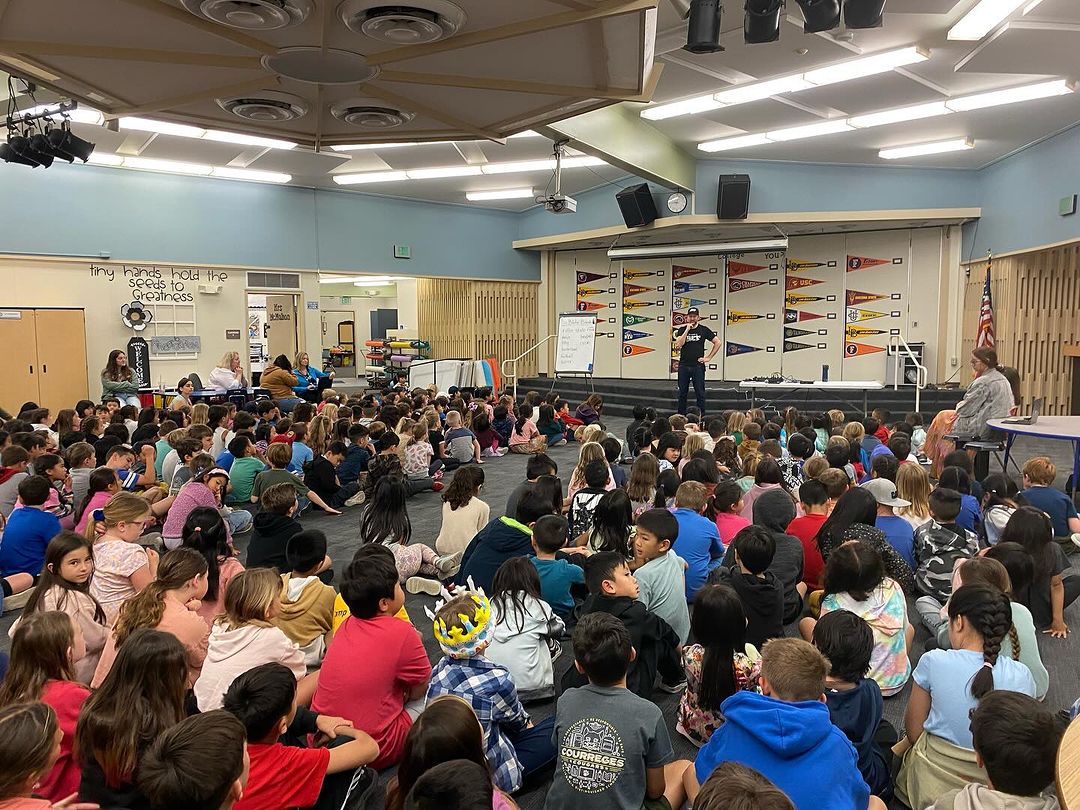 Auditorium full of students and teacher speaker at Courreges Elementary