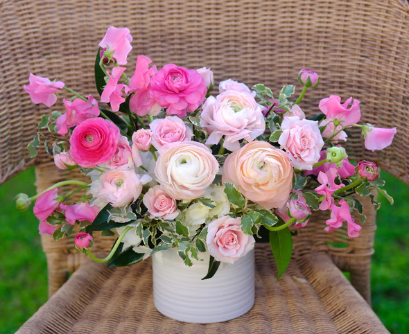 Beautiful Floral Arrangement in a white vase featuring ranunculus, spray roses, and sweet peas in a variety of pink shades alongside hydrangeas