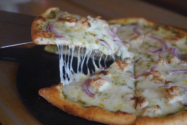 Close up view of sliced pizza with onions, sausage, and a green based pesto sauce from Sofra Urbana