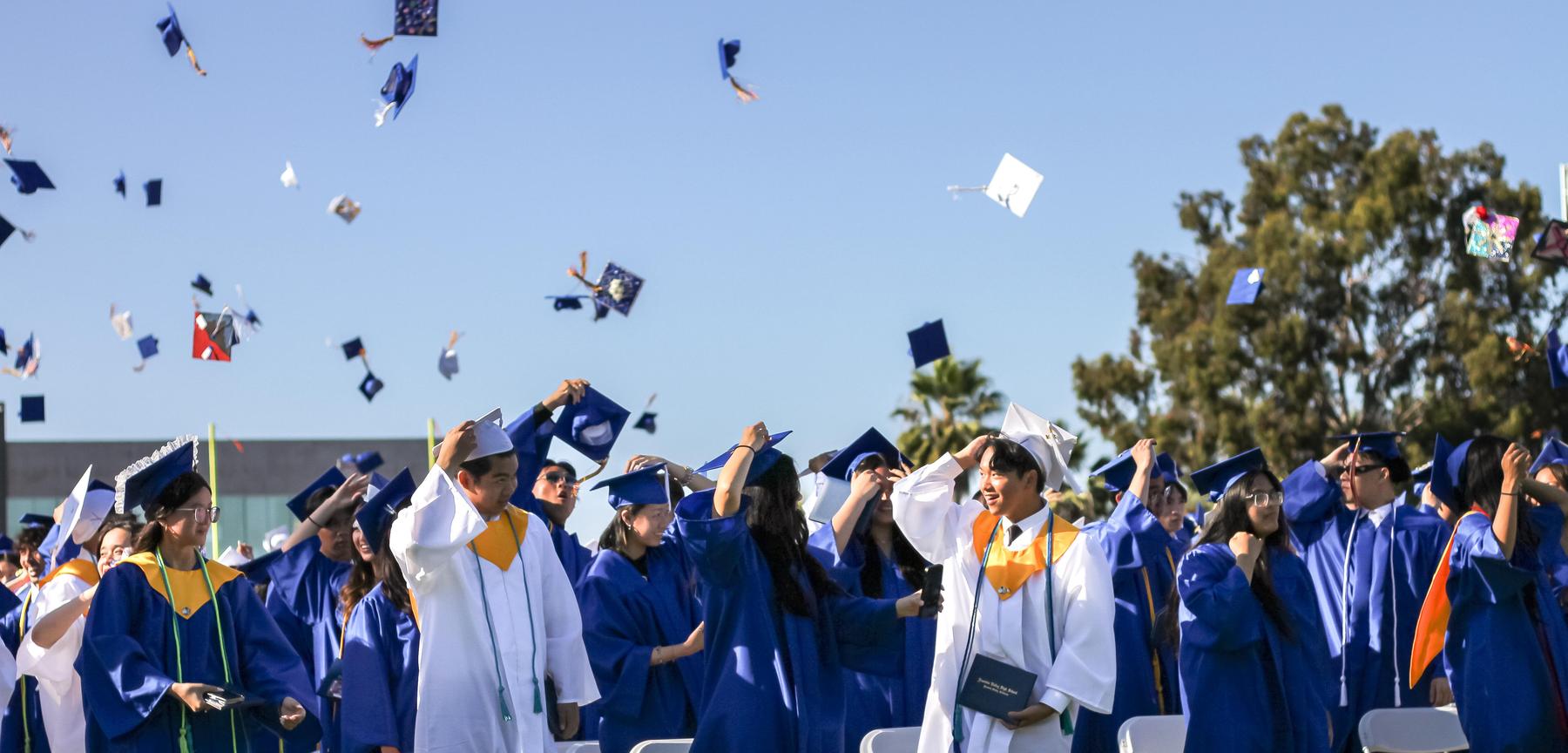 Graduating Class of High School Seniors in Blue and White Gowns, some throwing their caps in the air, at Fountain Valley High School