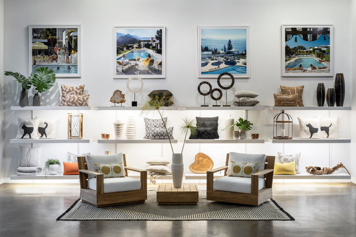 Interior of the Terra Outdoor Living showroom with two wood outdoor lounge chairs with white cushions, two throw pillows, and a bunch of outdoor furniture accents including vases, plants, and framed pictures