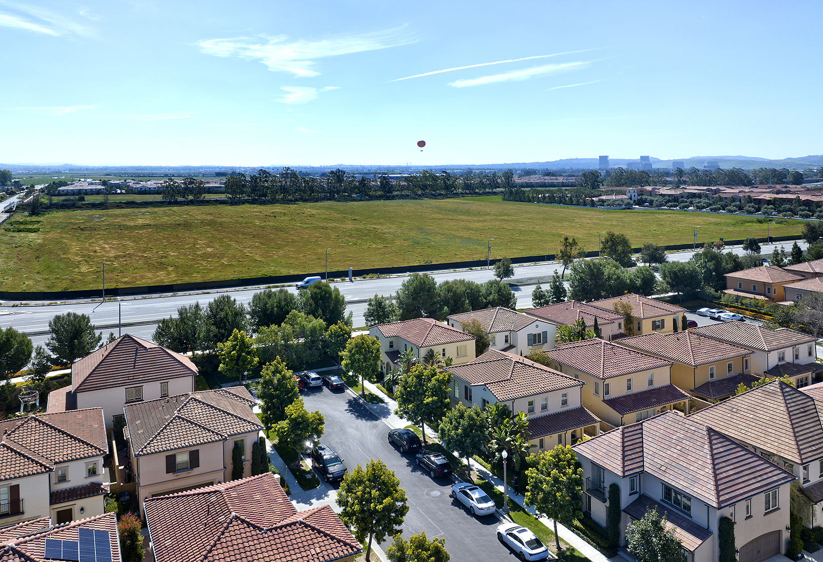 Drone shot of the Orange County Great Park, featuring green spaces, the iconic hot air balloon, and nearby townhomes