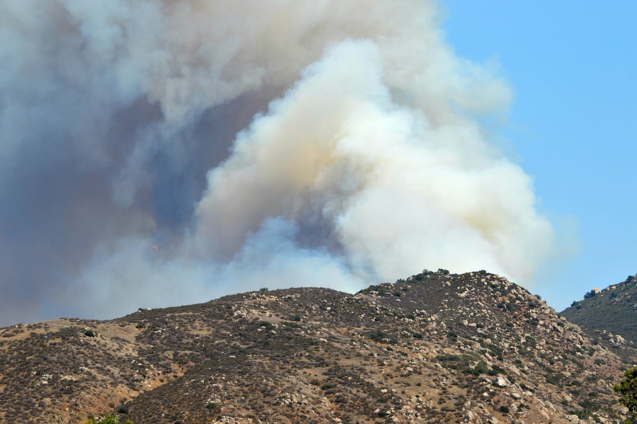 Smoke rises from an Orange County wildfire, highlighting the increased risk that has contributed to California's home insurance crisis. Laguna Hills homeowners face challenges finding affordable coverage, but the Brad Feldman Group, best Laguna Hills real estate agents, provide expert guidance.