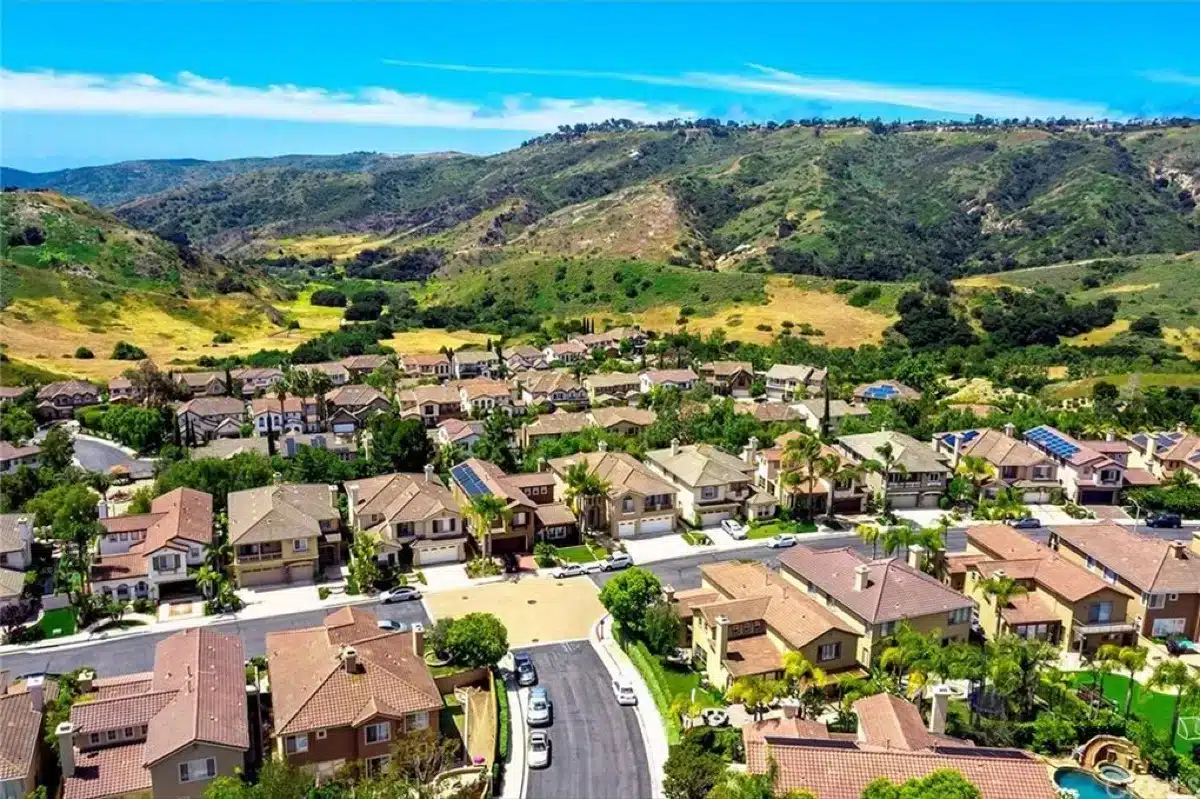 Scenic Aliso Viejo street with beautiful homes backed by rolling hills, showcasing the area's natural beauty and desirable real estate market in autumn.