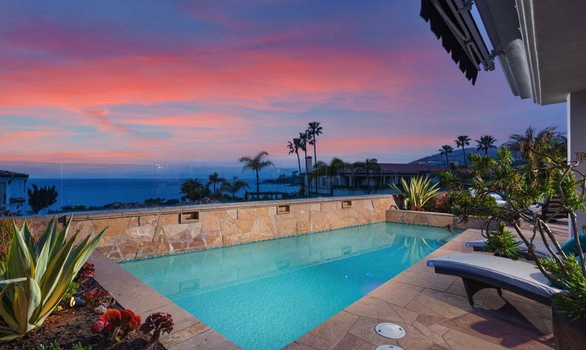 Backyard pool of Dana Point luxury home with views of the ocean at sunset, which you can also see from Laguna Niguel real estate for home buyers