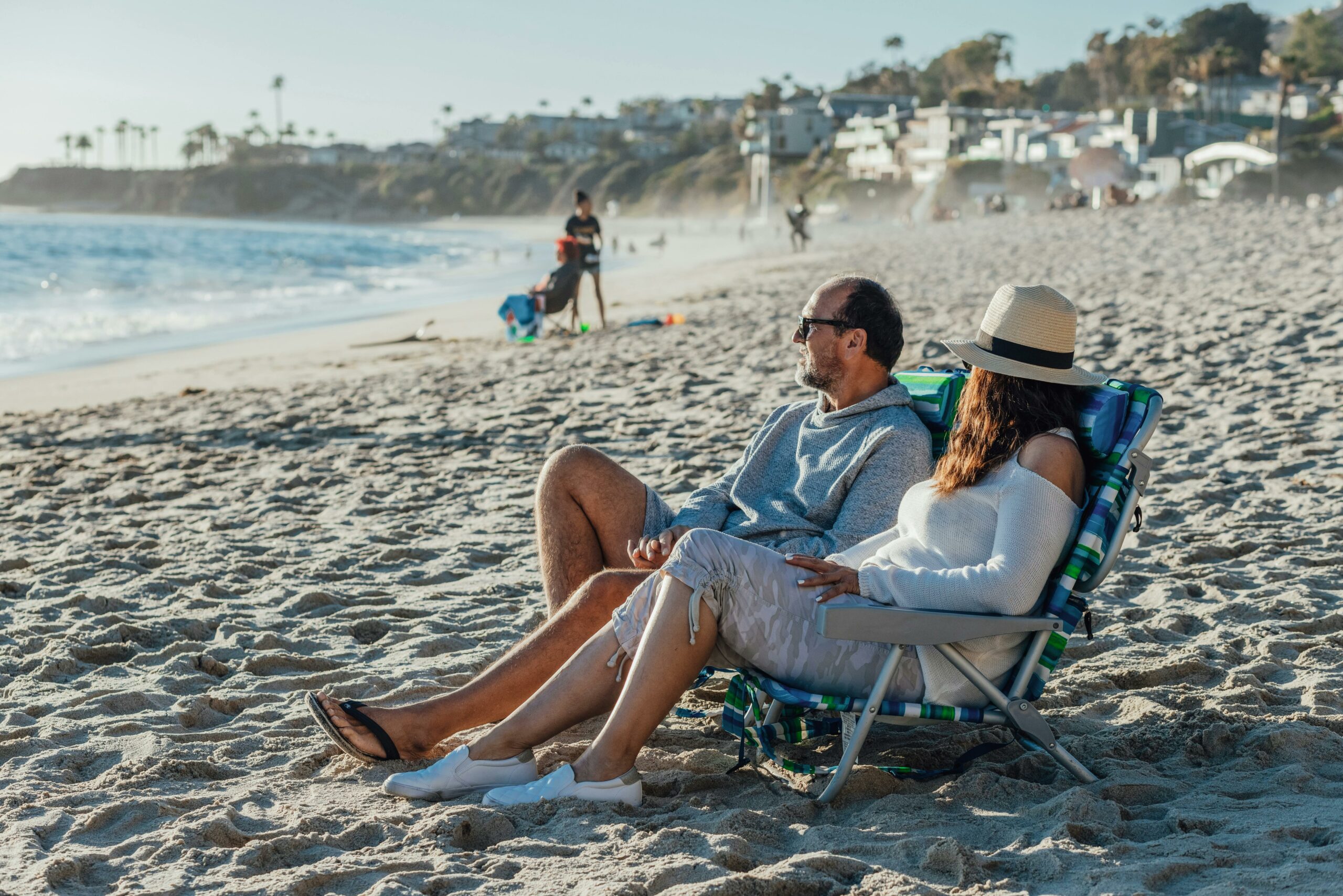 Couple relaxing on the sand of Laguna Beach real estate compared to Laguna Niguel for homebuyers
