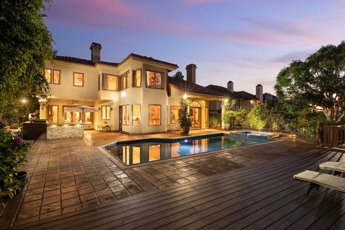 Backyard pool at dusk with deck and indoor lights on, listed by the Orange County real estate agents
