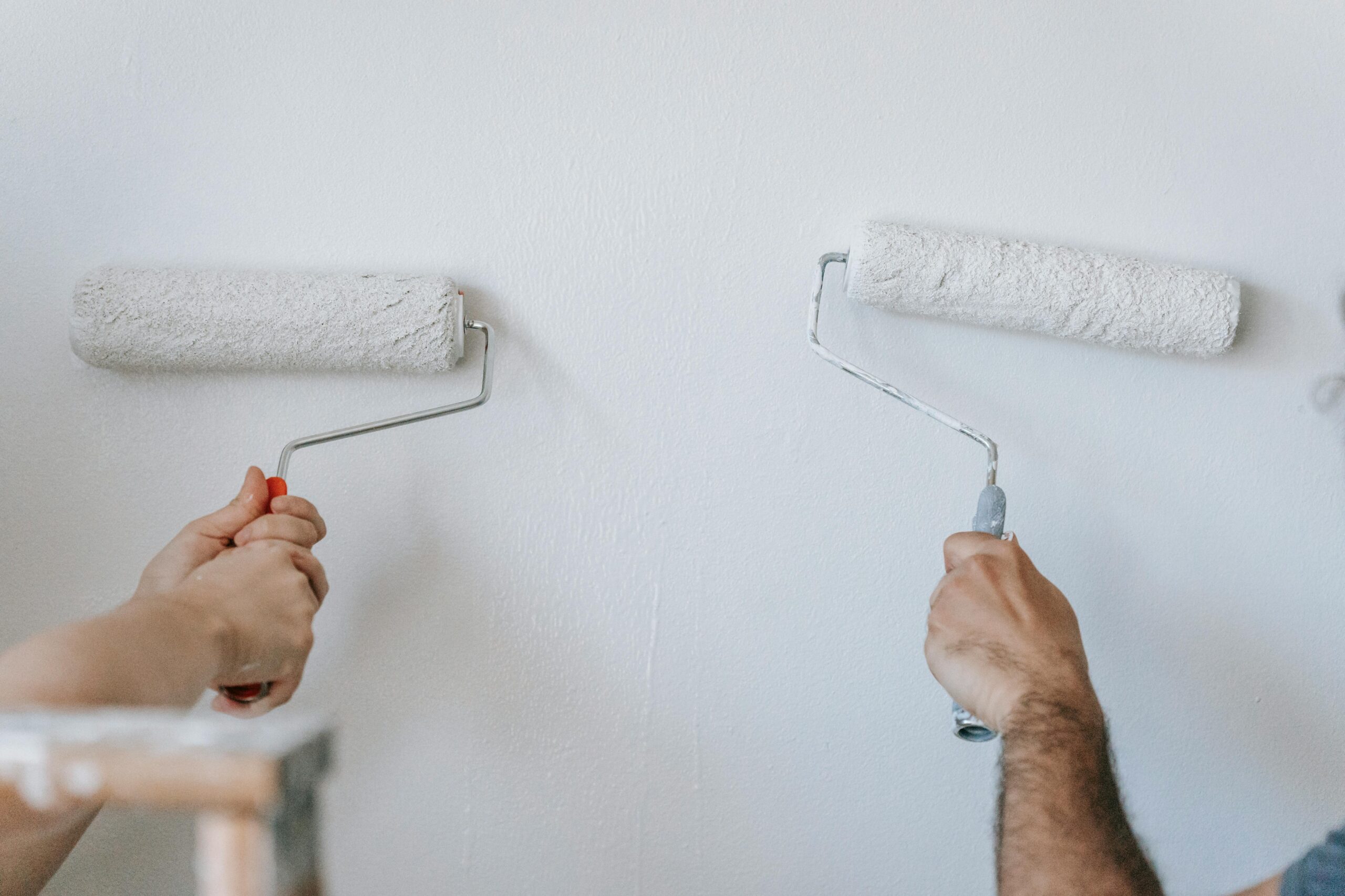 Two rollers on a wall with white paint representing the choice to sell as-is or update your Orange County home and real estate listing